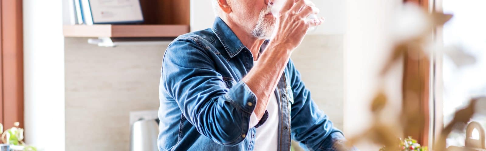 Senior man drinking water in the kitchen to prevent kidney stones | Urology Associates | Denver, CO