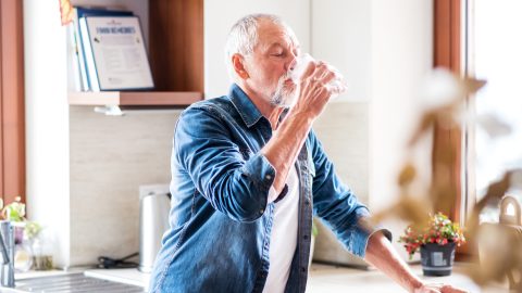 Senior man drinking water in the kitchen to prevent kidney stones | Urology Associates | Denver, CO
