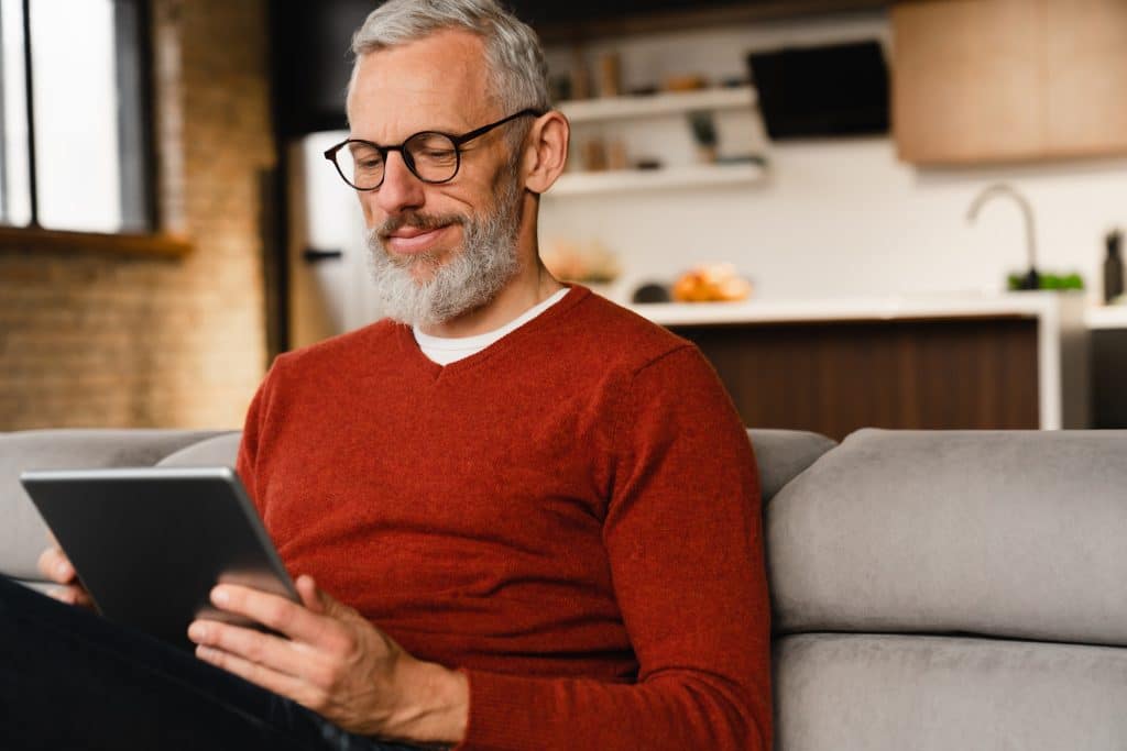 Closeup portrait of a smiling caucasian middle aged mature man in glasses using digital tablet for e learning, paying bills online, e commerce, remote work, social media online at home